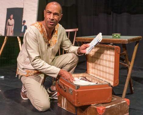 A man of dual heritage kneels next to an open suitcase of letters.